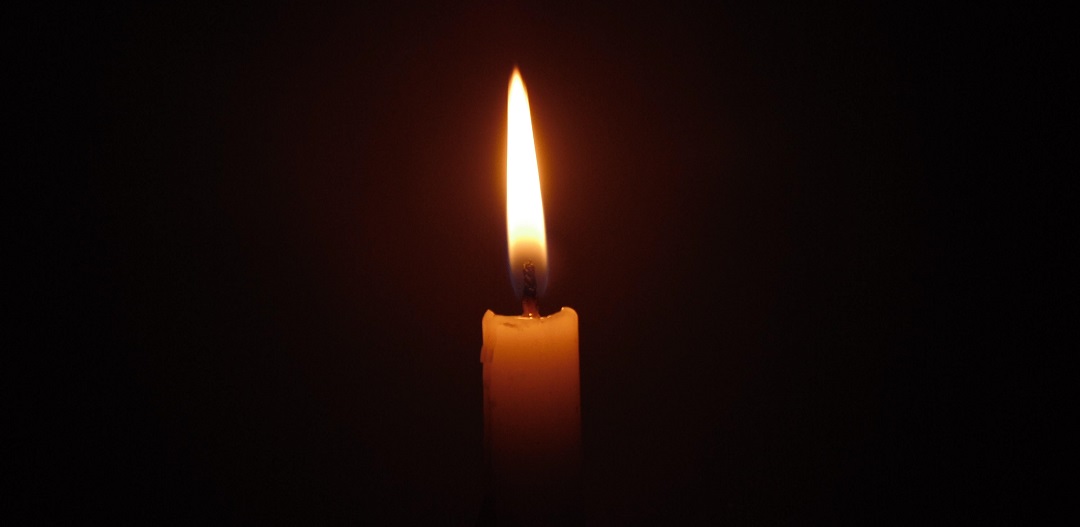 Single burning candle in darkness